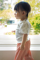 Full-body side profile of a baby girl walking in the Avauma summer floral t-shirt and pink pants.