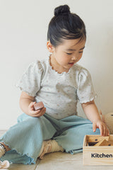 A young girl sitting and playing while wearing the Avauma grey floral tee paired with teal wide-leg ribbed pants.