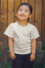 Smiling toddler modeling the Avauma summer floral t-shirt and black relaxed-fit trousers in an outdoor garden setting.