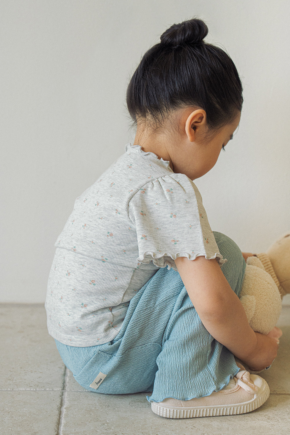 Side view of a child squatting to play, showcasing the comfortable fit of the Avauma heather grey floral top and teal pants.