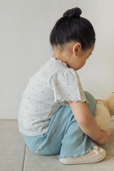 Side view of a child squatting to play, showcasing the comfortable fit of the Avauma heather grey floral top and teal pants.
