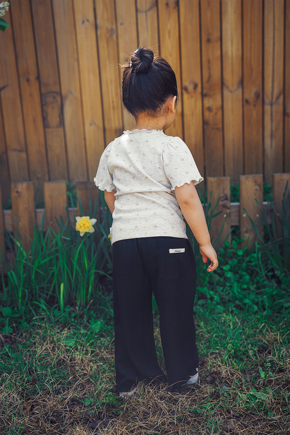 Back view of the Avauma toddler outfit featuring the floral ruffled tee and black pants with a signature brand label on the pocket.