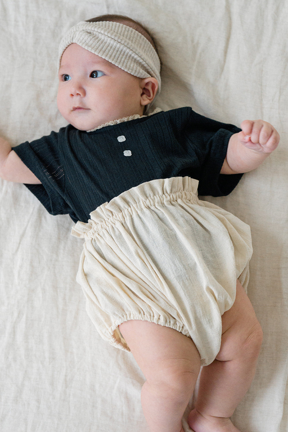 Baby wearing Avauma Soft Ivory Berry Puff Bloomer with elastic ruffles, styled with dark top and beige textured headband
