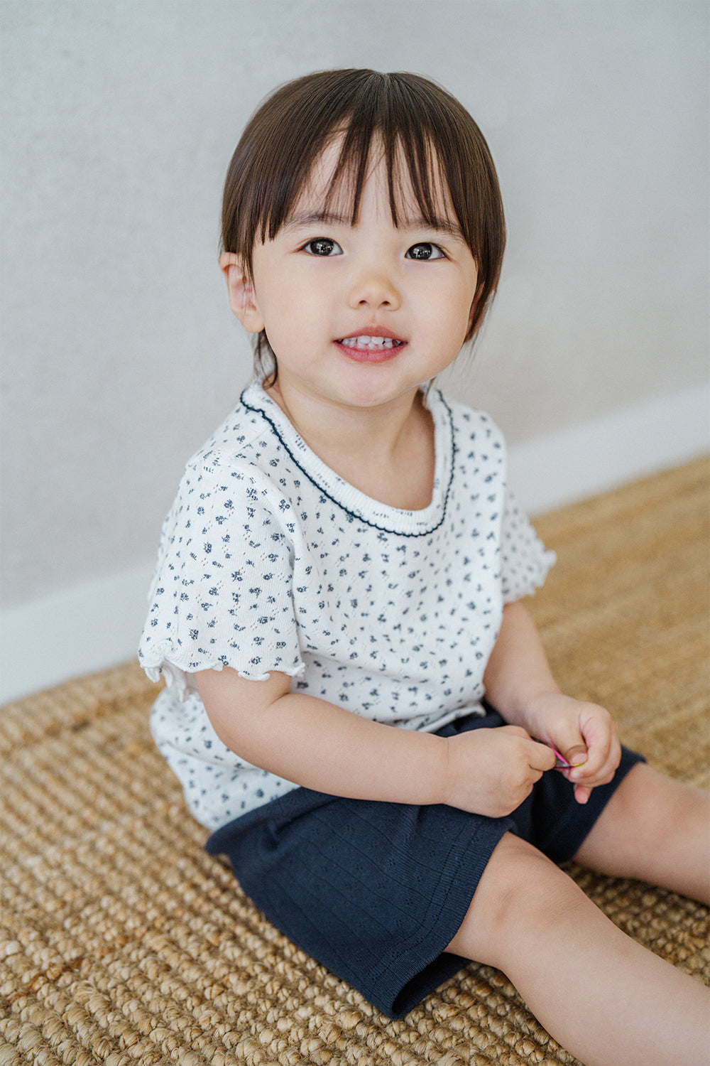 Avauma breeze garden baby setup indigo whisper - toddler smiling in white floral t-shirt and navy shorts sitting on rug

