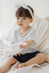 Avauma breeze garden baby setup indigo whisper - girl with headband holding plush toy in white floral top and navy shorts on bed

