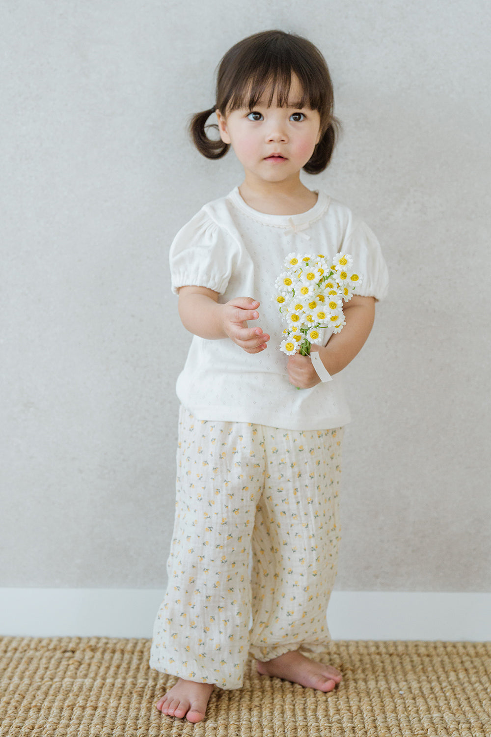  Girl wearing Avauma Breeze Jogger Pants in yellow flower print, standing barefoot on woven mat.