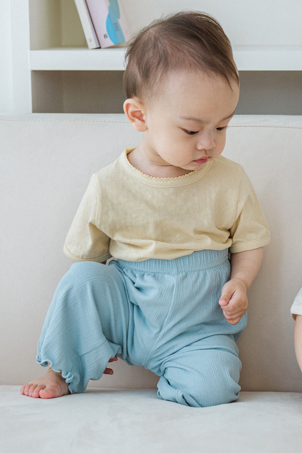 Baby in beige lace short sleeve top and blue pants, looking down – Avauma

