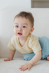 Smiling baby in Avauma oat beige lace short sleeve t-shirt and blue pants, crawling on sofa

