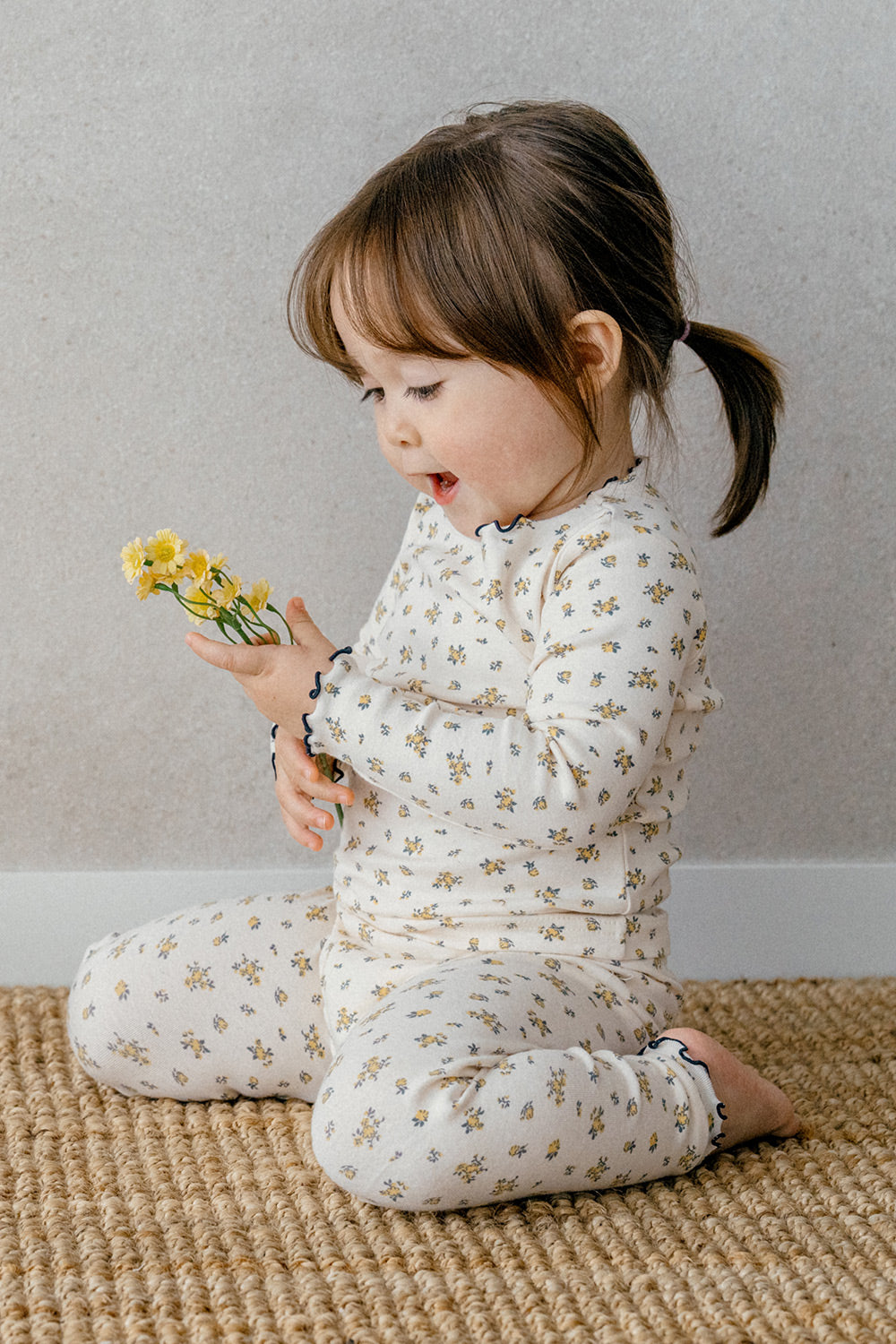 Baby standing in a crib, dressed in Avauma Fluid Blossom Long Sleeve Baby Pajamas - Strawberry Milk, highlighting the cozy pink pajama set with delicate floral designs.