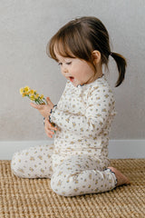 Baby standing in a crib, dressed in Avauma Fluid Blossom Long Sleeve Baby Pajamas - Strawberry Milk, highlighting the cozy pink pajama set with delicate floral designs.