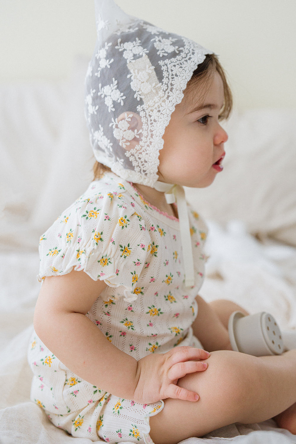 Side view of baby in Avauma Petite Ruffle Short Sleeve Set - Honey Daisy, playing with toy, highlighting cute ruffle sleeves and daisy pattern.

