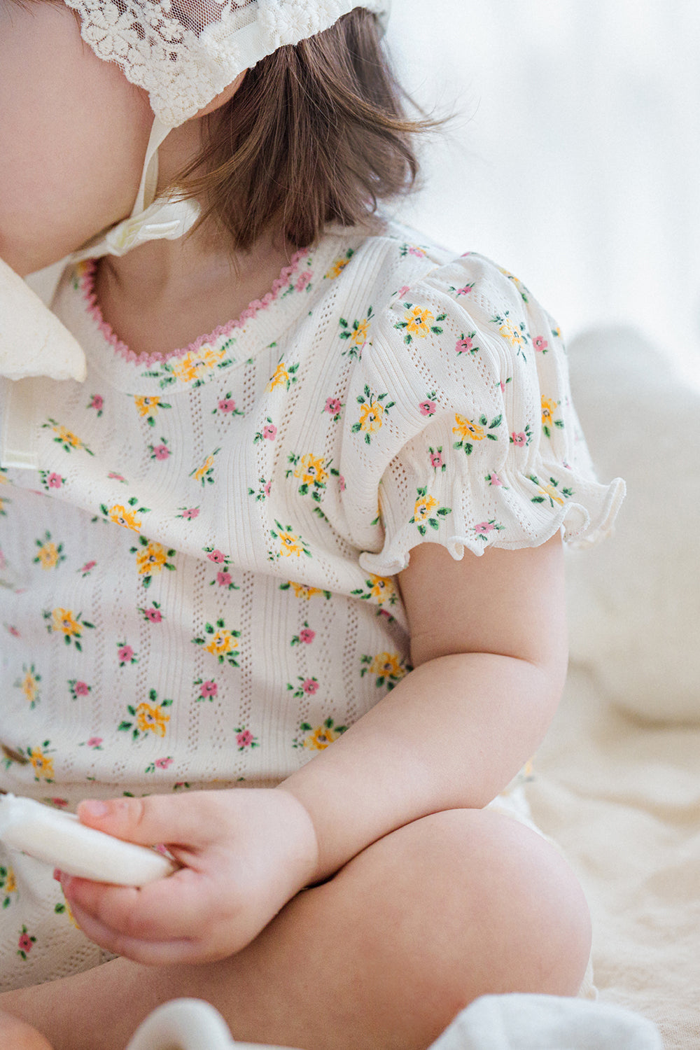 Detail view of baby in Avauma Petite Ruffle Short Sleeve Set - Honey Daisy, showcasing soft ruffle sleeves and yellow-pink floral print.

