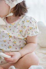 Detail view of baby in Avauma Petite Ruffle Short Sleeve Set - Honey Daisy, showcasing soft ruffle sleeves and yellow-pink floral print.

