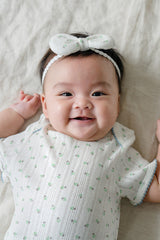 Smiling baby girl wearing Avauma Petite Garden Baby Headband in Mint Garden with green floral print, lying on a blanket