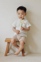 A toddler boy sitting on a wooden stool wearing Avauma honey beige floral t-shirt and shorts.