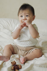 A baby sitting on a striped bed wearing Avauma honey beige floral top and ribbed bottom.