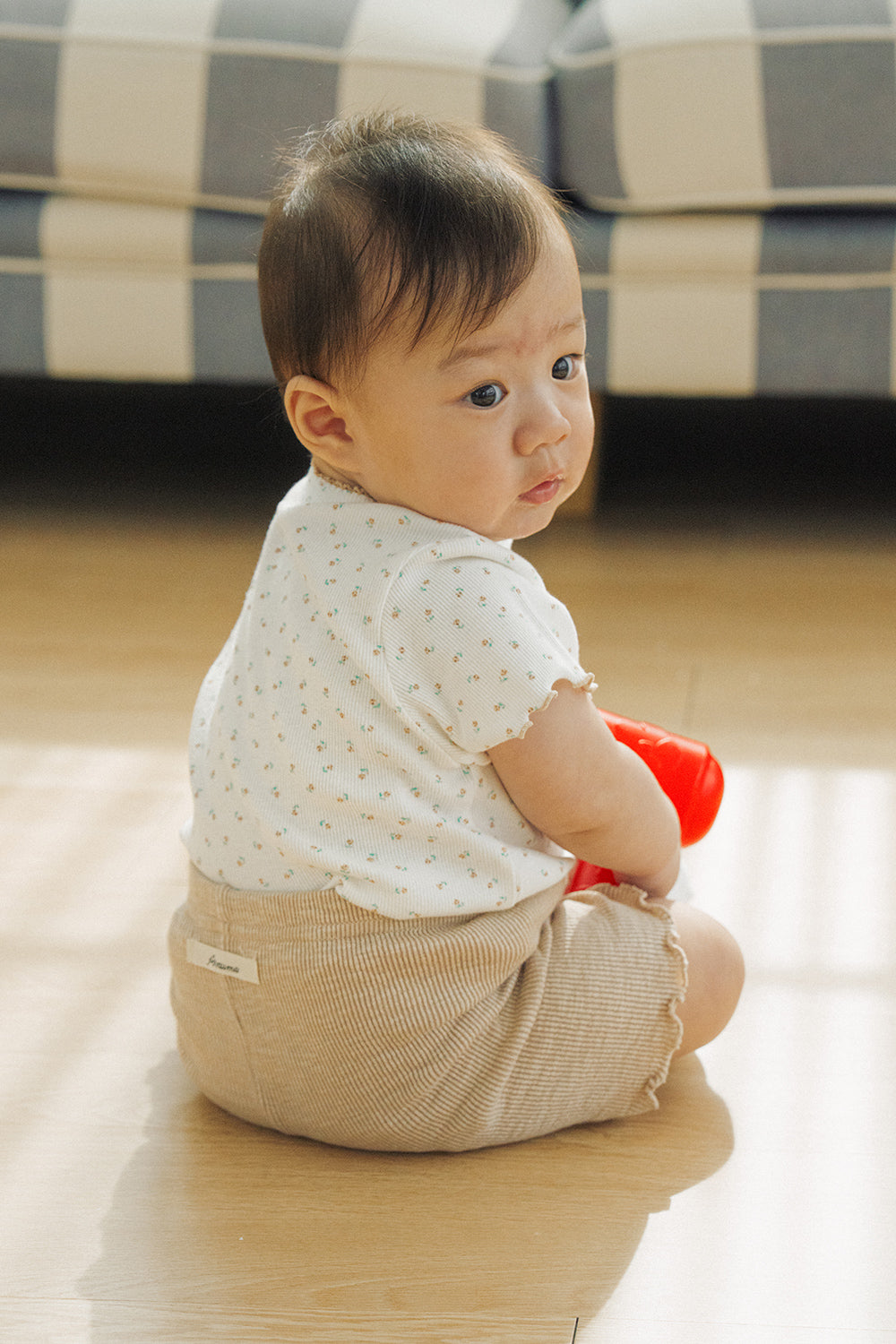 Side view of a baby sitting on the floor in Avauma honey beige floral setup with ribbed texture.