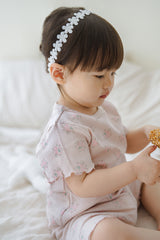 A baby girl playing on a bed, wearing Avauma Sienna Rose Rosy Powder floral ruffle set, captured in a soft and natural light.