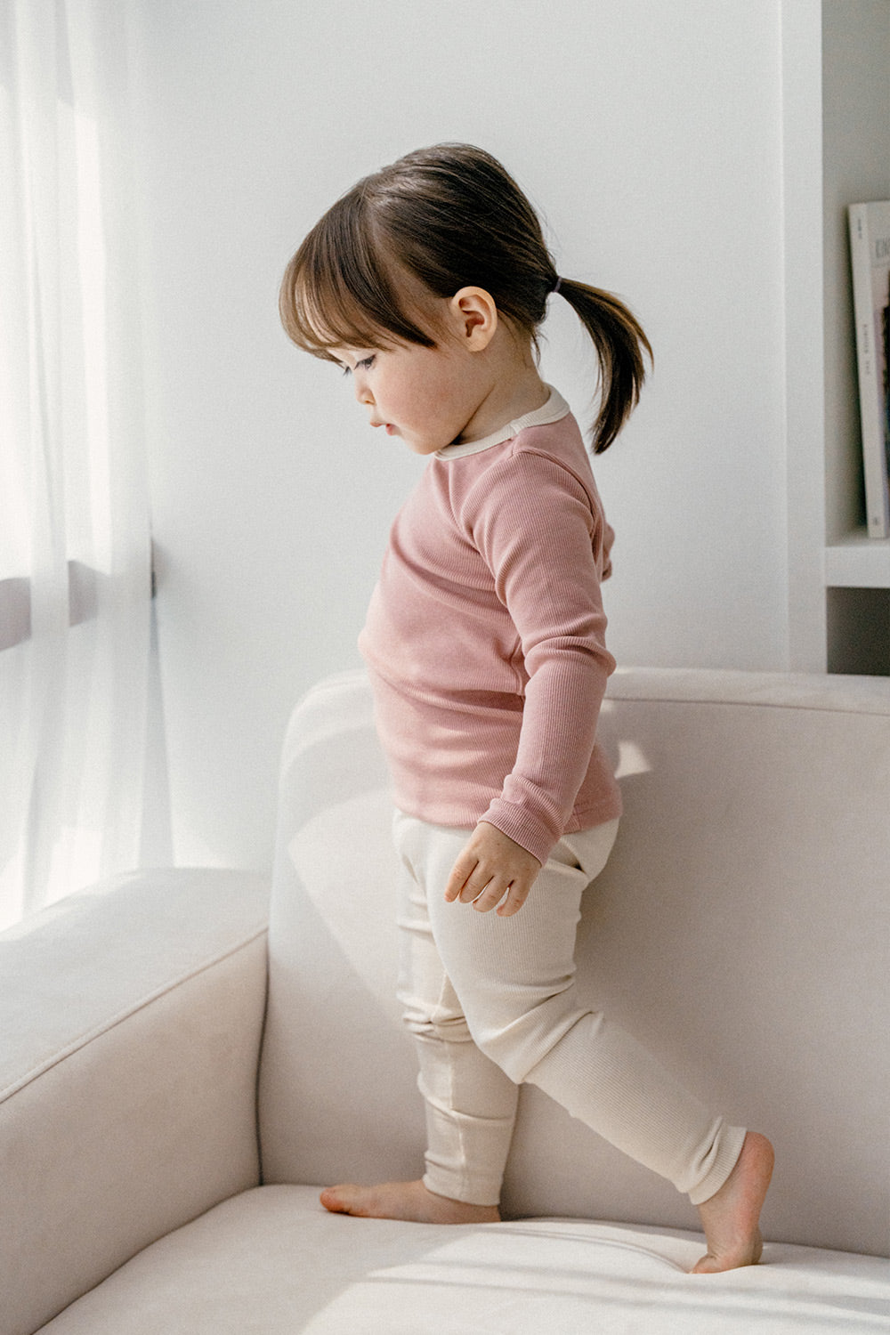 Toddler standing on a couch wearing Avauma's Coco Classic Long Sleeve Set in Strawberry Cheese color - comfortable baby pajamas for both sleep and play.