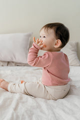 Baby sitting on a bed in Avauma's Coco Classic Long Sleeve Set in Strawberry Cheese color - breathable and soft baby sleepwear, ideal for all-day comfort.