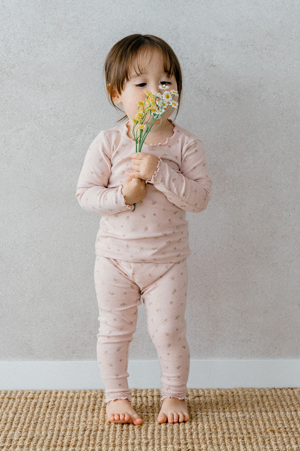 Toddler girl wearing Avauma Fluid Blossom Long Sleeve Baby Pajamas - Strawberry Milk, a light pink pajama set with soft floral patterns and frill accents on the collar and sleeves.