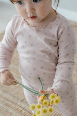 Close-up of a toddler wearing Avauma Fluid Blossom Long Sleeve Baby Pajamas - Strawberry Milk, showing the detailed floral print and frill trim on soft pink fabric.