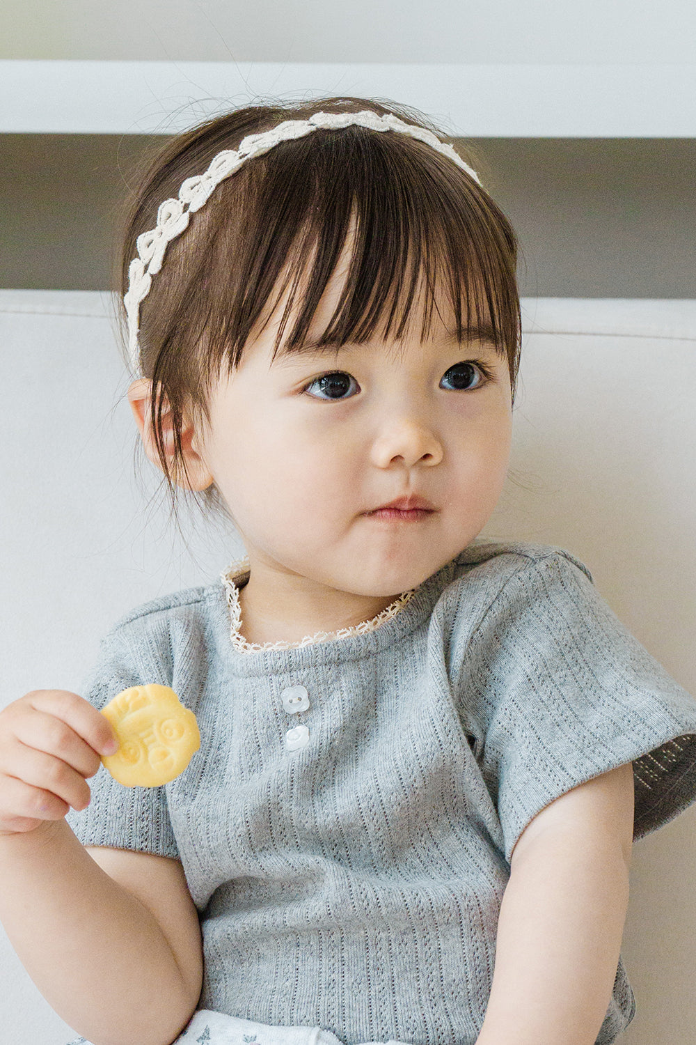 Toddler holding cookie while wearing Avauma White Garden Band in Cream Beige and a gray knit top