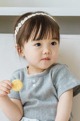 Toddler holding cookie while wearing Avauma White Garden Band in Cream Beige and a gray knit top