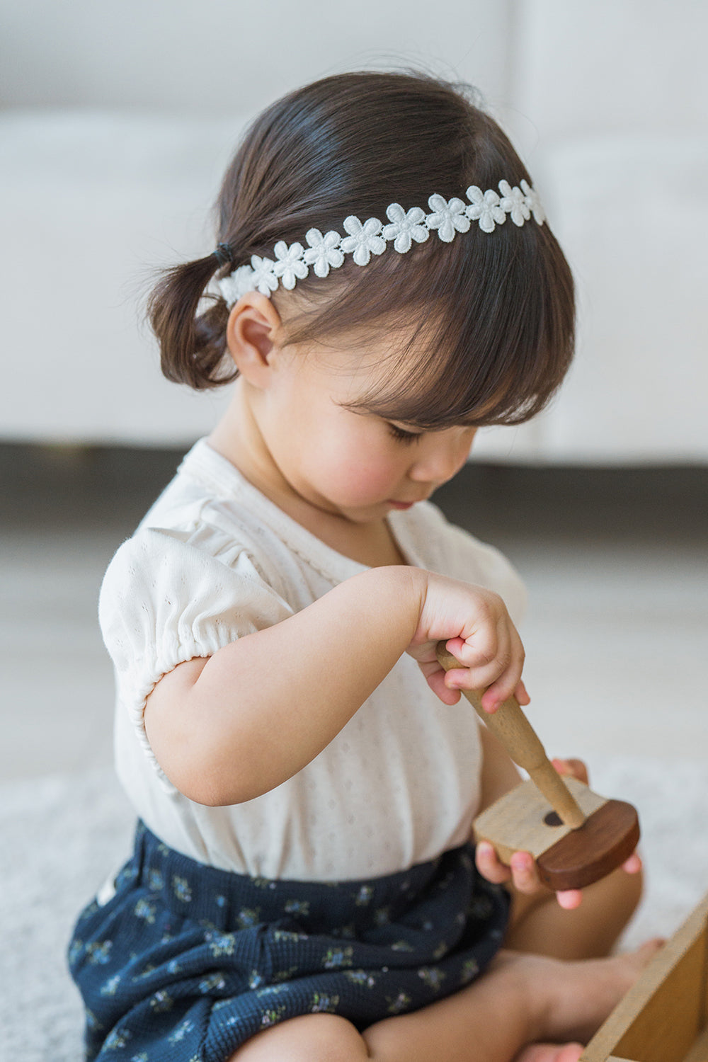 Toddler playing with toy while wearing Avauma White Garden Band headband in Pure White